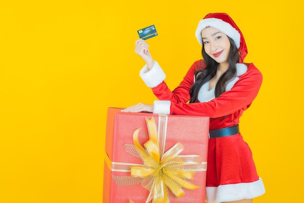 Porträt schöne junge asiatische Frau trägt Weihnachtskostüm mit roter Geschenkbox auf Gelb