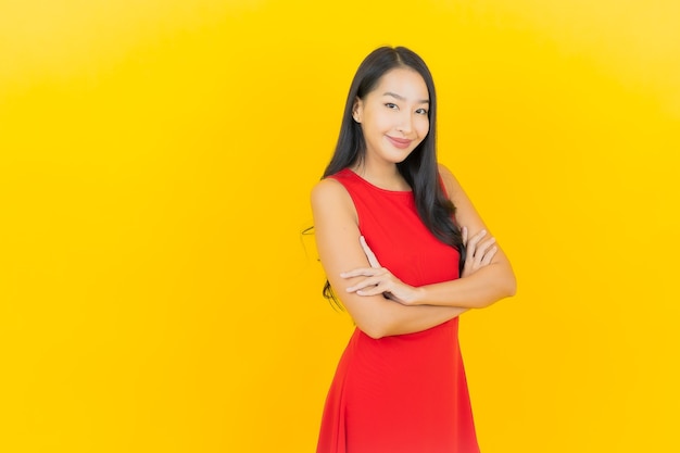 Porträt schöne junge asiatische Frau tragen rotes Kleid Lächeln mit Aktion auf gelber Wand