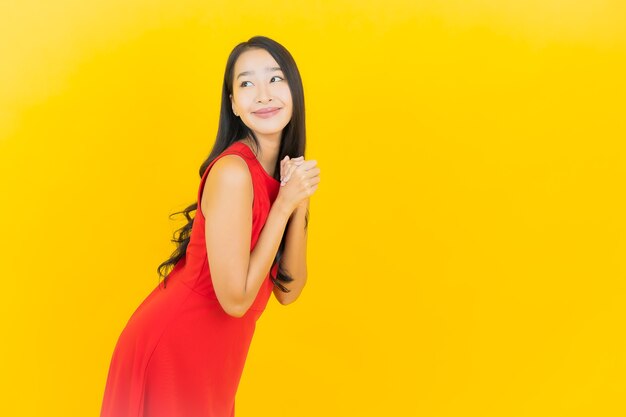 Porträt schöne junge asiatische Frau tragen rotes Kleid Lächeln mit Aktion auf gelber Wand