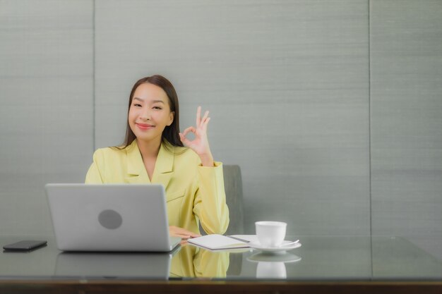 Porträt schöne junge asiatische Frau verwenden Computer-Laptop mit Smart-Handy auf Arbeitstisch im Innenraum