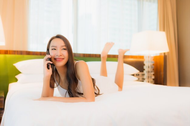 Porträt schöne junge asiatische frau verwenden smartphone auf dem bett im schlafzimmer interieur