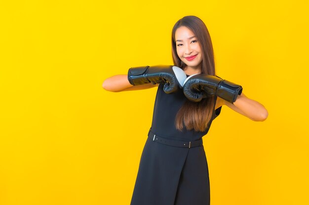 Porträt schöne junge asiatische Geschäftsfrau mit Boxhandschuh auf gelbem Hintergrund