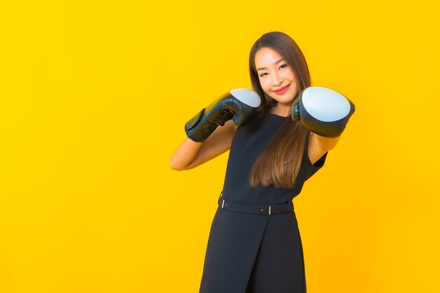 Porträt schöne junge asiatische Geschäftsfrau mit Boxhandschuh auf gelbem Hintergrund