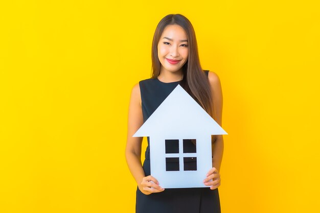 Porträt schöne junge asiatische Geschäftsfrau mit Hauspapierschild auf gelbem Hintergrund