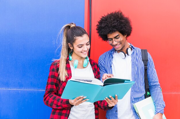 Porträt von den glücklichen jungen Paaren, die zusammen stehen, gegen rote und blaue Wand stehend