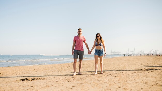 Porträt von den jungen Paaren, welche die Hand von einander genießen, die am Strand genießt