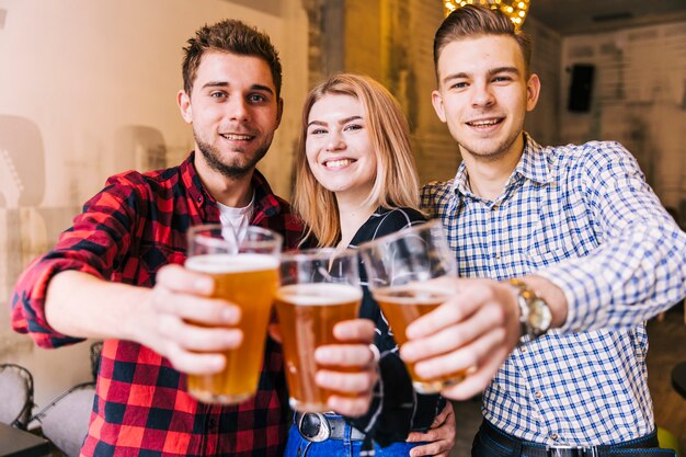 Porträt von den lächelnden jungen Freunden, welche die Biergläser rösten