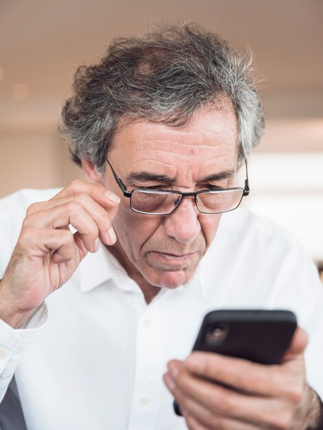 Porträt von den tragenden Brillen des älteren Mannes, die Handy betrachten