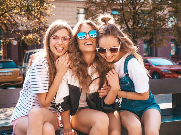 Porträt von drei jungen schönen lächelnden Hippie-Mädchen in der modischen Sommerkleidung. Sexy sorglose Frauen, die auf der Straße aufwerfen Positive Modelle, die Spaß in der Sonnenbrille haben umarmen