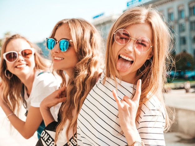 Porträt von drei jungen schönen lächelnden Hippie-Mädchen in der modischen Sommerkleidung. Sexy sorglose Frauen, die auf der Straße aufwerfen Positive Modelle, die Spaß in der Sonnenbrille haben Zeigt Rock-and-Rollzeichen