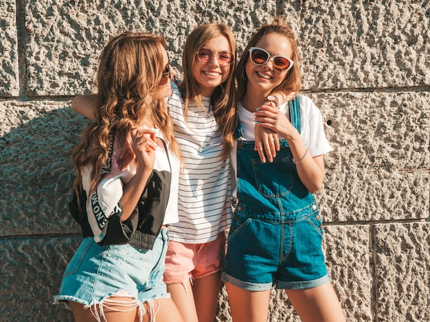 Porträt von drei jungen schönen lächelnden Hippie-Mädchen in der modischen Sommerkleidung. Sexy sorglose Frauen, die nahe Wand in der Straße aufwerfen Positive Modelle, die Spaß in der Sonnenbrille haben