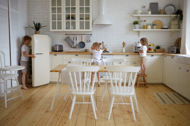 Porträt von drei unabhängigen Kindergeschwistern, die das Abendessen selbst vorbereiten, während die Eltern bei der Arbeit sind. Kinder machen gemeinsam Frühstück in der Küche. Konzept für Essen, Küche, Küche, Kindheit und Ernährung