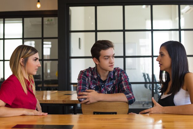 Porträt von ernsten Studentenfreunden, die bei Tisch sitzen und sprechen