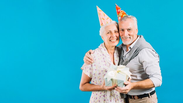 Porträt von glücklichen älteren Paaren mit Geburtstagsgeschenk auf blauem Hintergrund