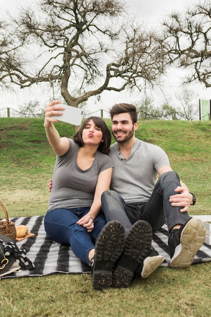 Porträt von glücklichen jungen Paaren auf dem Picknick, das selfie am Handy nimmt