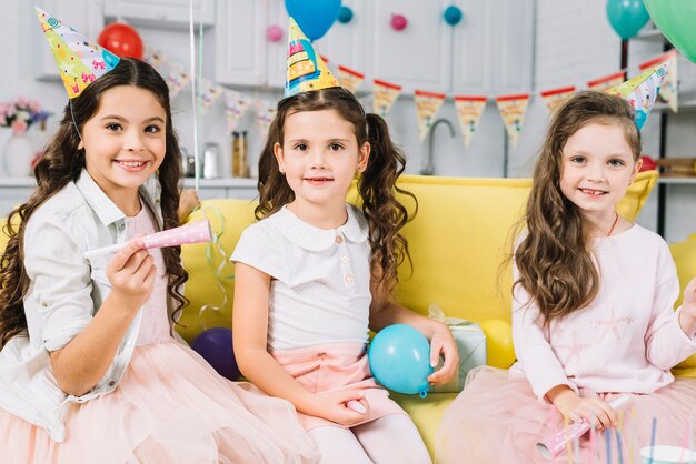 Porträt von glücklichen Mädchen mit dem Ballon- und Partyhorn, das auf Sofa sitzt
