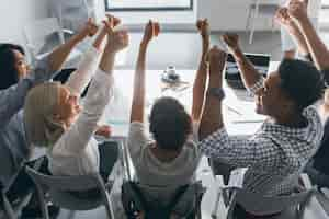 Kostenloses Foto porträt von hinten von fröhlichen schülern, die zusammen am tisch sitzen und hände heben. innenfoto des teams von freiberuflichen spezialisten, die spaß nach harter arbeit im büro haben.