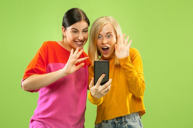 Porträt von hübschen charmanten Mädchen in lässigen Outfits lokalisiert auf grüner Wand. Freundinnen oder Lesben machen Selfie. Konzept von LGBT, Gleichheit, menschlichen Emotionen, Liebe, Beziehung.