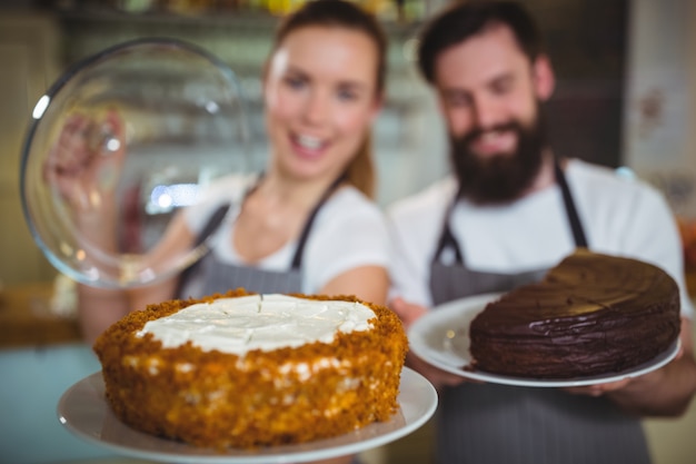 Porträt von Kellner und Kellnerin, die einen Teller mit Kuchen halten