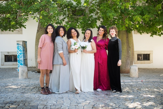 Porträt von lächelnden Bräuten und Gästen bei der Hochzeit. Frauen verschiedener Nationalitäten in festlichen Kleidern stehen zusammen