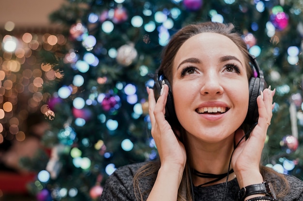 Porträt von lächelnden tragenden Kopfhörern der Frau nahe Weihnachtsbaum