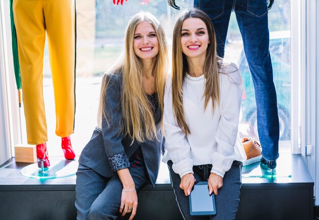 Porträt von zwei Freundinnen, die im Kleidungsspeicher mit digitaler Tablette sitzen