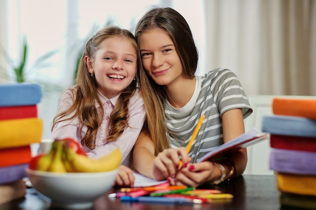 Porträt von zwei Freundinnen, die mit vielen Büchern am Tisch studieren.