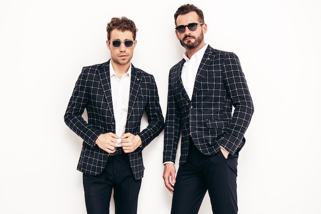 Porträt von zwei gutaussehenden, selbstbewussten, stilvollen Hipster-Lambersexual-Modellen Sexy moderne Männer in schwarzem, elegantem Anzug Modemann posiert im Studio in der Nähe einer weißen Wand mit Sonnenbrille