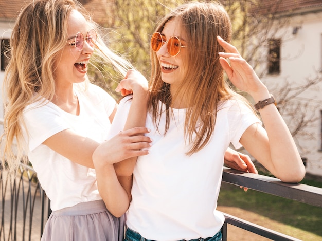 Porträt von zwei jungen schönen blonden lächelnden Hippie-Mädchen im weißen T-Shirt des modischen Sommers kleidet. . Positive Modelle, die Spaß in der Sonnenbrille haben