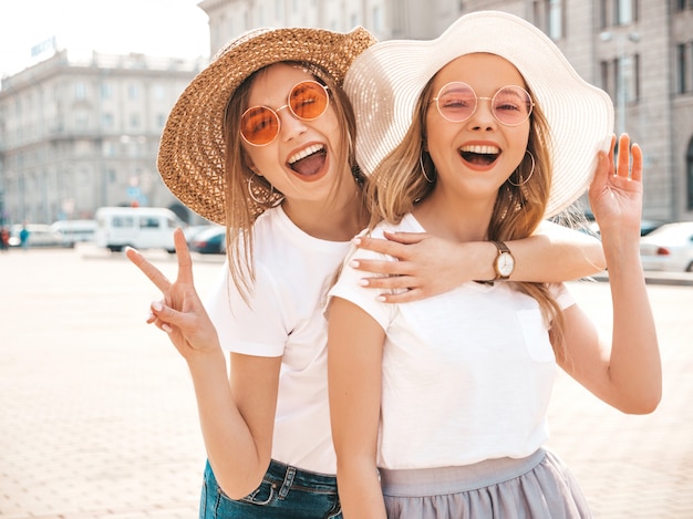 Porträt von zwei jungen schönen blonden lächelnden Hippie-Mädchen im weißen T-Shirt des modischen Sommers kleidet.
