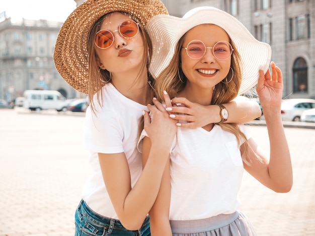 Porträt von zwei jungen schönen blonden lächelnden Hippie-Mädchen im weißen T-Shirt des modischen Sommers kleidet.