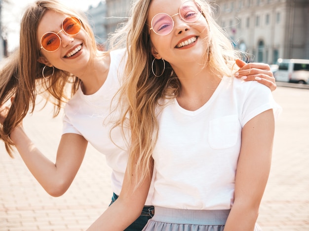 Porträt von zwei jungen schönen blonden lächelnden Hippie-Mädchen im weißen T-Shirt des modischen Sommers kleidet.