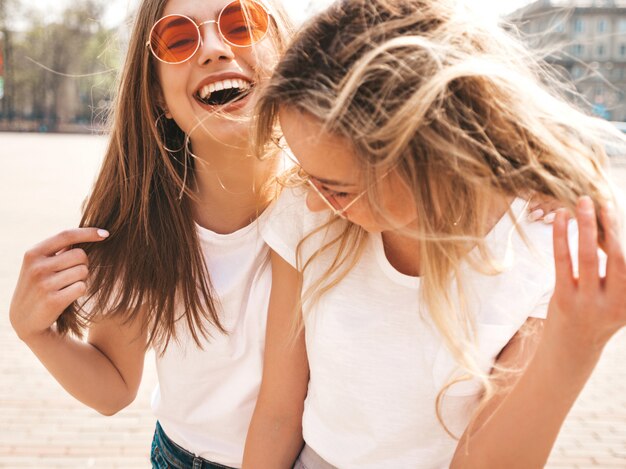 Porträt von zwei jungen schönen blonden lächelnden Hippie-Mädchen im weißen T-Shirt des modischen Sommers kleidet.