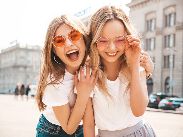 Porträt von zwei jungen schönen blonden lächelnden Hippie-Mädchen im weißen T-Shirt des modischen Sommers kleidet.