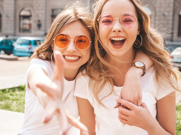 Porträt von zwei jungen schönen blonden lächelnden Hippie-Mädchen im weißen T-Shirt des modischen Sommers kleidet.