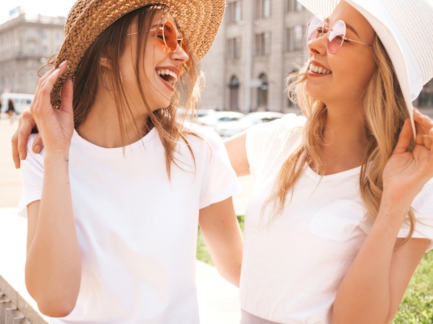 Porträt von zwei jungen schönen blonden lächelnden Hippie-Mädchen im weißen T-Shirt des modischen Sommers kleidet.