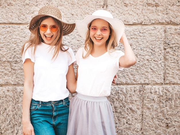 Porträt von zwei jungen schönen blonden lächelnden Hippie-Mädchen im weißen T-Shirt des modischen Sommers kleidet.