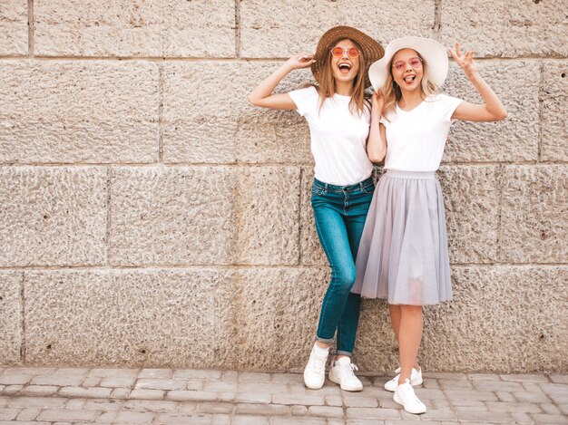 Porträt von zwei jungen schönen blonden lächelnden Hippie-Mädchen im weißen T-Shirt des modischen Sommers kleidet.