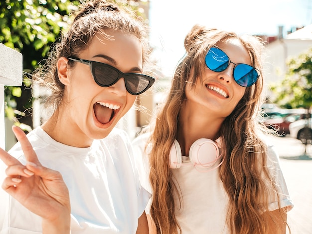 Porträt von zwei jungen schönen lächelnden Hippie-Frauen in trendiger weißer Sommer-T-Shirt-Kleidung