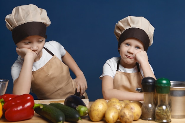 Kostenloses Foto porträt von zwei kleinen jungen in kochuniform mit gelangweilten blicken