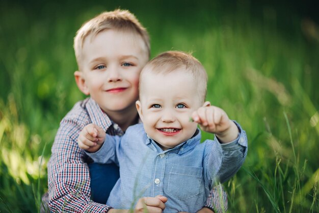 Porträt von zwei kleinen, stilvollen, glücklichen Brüdern mit schönen blauen Augen, die im Park spielen, sich umarmen und in die Kamera schauen Jungen, die Hemden tragen, die vor grünem Grashintergrund posieren