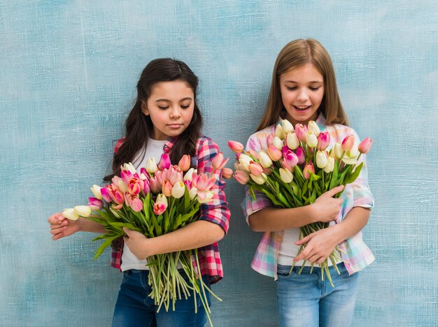 Porträt von zwei Mädchen, die vor der blauen Wand hält Tulpenblumenblumenstrauß stehen