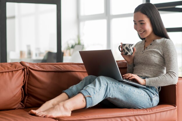 Porträtfrau, die Tee trinkt und Laptop verwendet