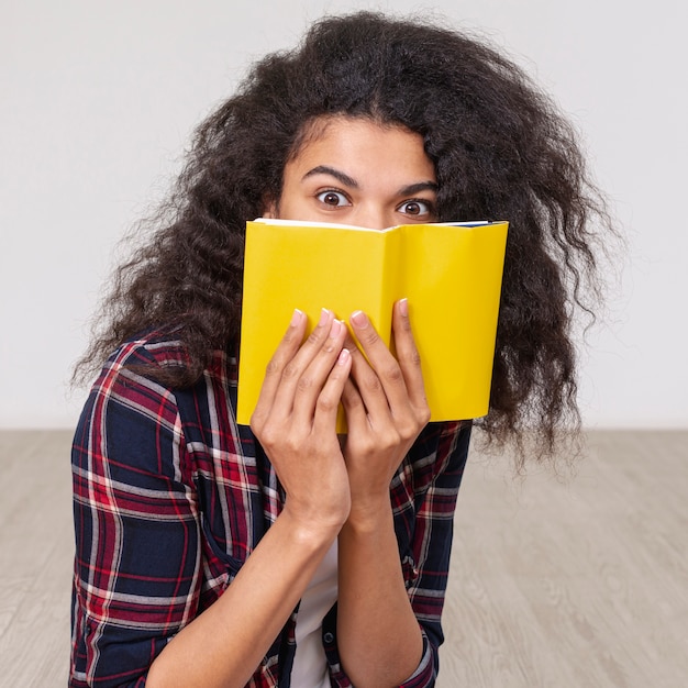 Porträtmädchen, das ihr Gesicht mit Buch bedeckt