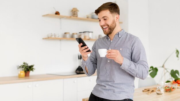 Porträtmann, der Kaffee trinkt, während Handy überprüft