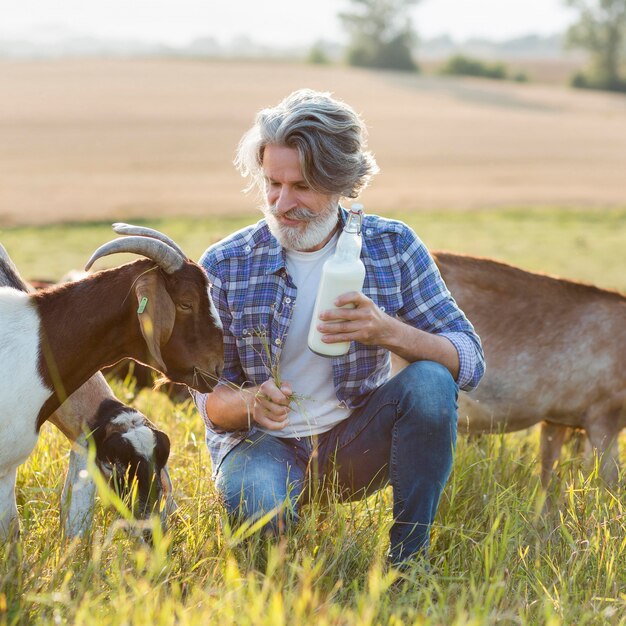 Porträtmann neben Ziegen mit Flasche Milch