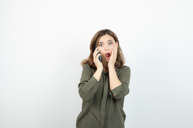 Portrait der entzückenden Frau, die über Mobiltelefon über Weiß spricht. Foto in hoher Qualität