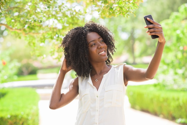 Portrait der fröhlichen Frau, die selfie im Park nimmt