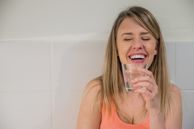 Kostenloses Foto portrait der glücklichen jungen frau trinken wasser gegen küche hintergrund. gesunder lebensstil. gesundheitswesen. trinken gesundheit, schönheit, diät-konzept. gesundes essen.