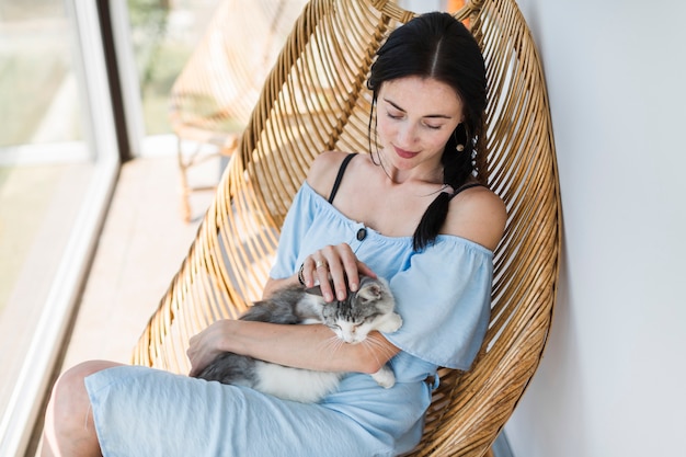 Portrait der jungen Frau sitzend auf dem Stuhl, der ihre Katze streicht